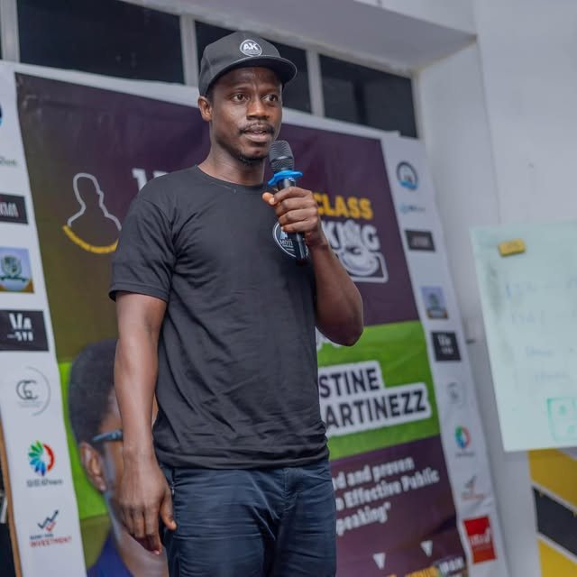 Abdulai in an AK cap holding a microphone at a public speaking event